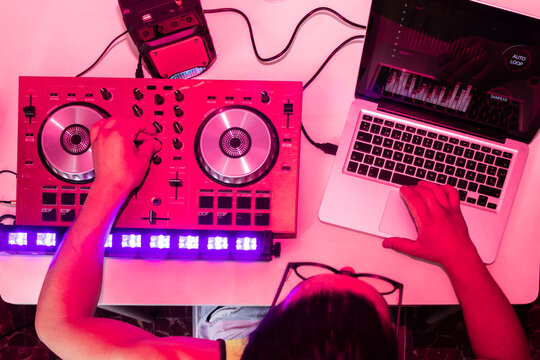 DJ mixes tracks on modern equipment under pink lights
