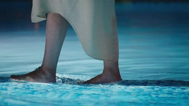 Elegant woman in dress walks at poolside illuminated at night, slow motion cinematic isolated shot