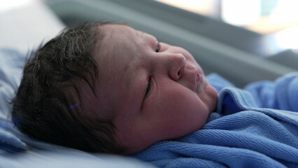 Infant newborn baby close-up face initial days right after birth, first day of a human being in the...