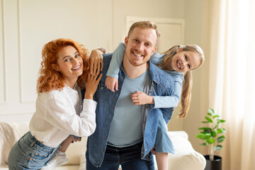 Spending time with family. Portrait of excited man, woman and girl laughing and posing at home in living room