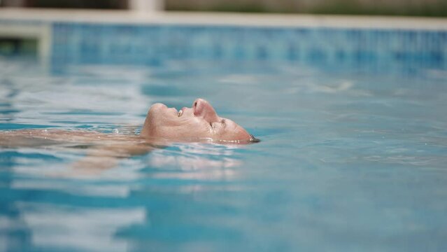Man floating on his back in swimming pool with only his face visible, enjoying a peaceful moment on a sunny day at summer vacation beach
