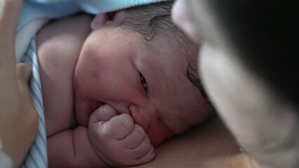 Newborn close-up face right after birth, minutes moments after childbirth arriving at the world resting on mother's skin to skin contact