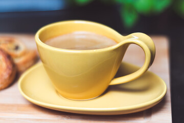Yellow cup with coffee and crosant on a plate set on a wooden board, breakfast time, French breakfast, coffee break