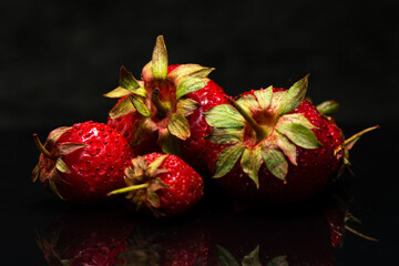 Fototapeta premium Fresh ripe natural strawberries on a black background. Freshly picked garden strawberries. Detailed photo of strawberries on an abstract background. Close up view.