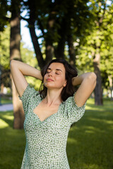 Fototapeta premium Young brunette woman enjoying sun with eyes closed in summer green park