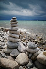 Pebble tower, stones, in the sun's beam, on the seashore or lake against the background of water and dramatic thunderstorm sky. Balance, place for meditation and rest.