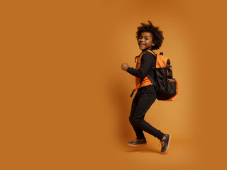 Run out cheerful black african american boy, afro haircut, backpack, orange isolated background