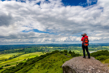 Hiker taking a photograph from a hill overlooking rolling farmland (Brecon Beacons, Wales)