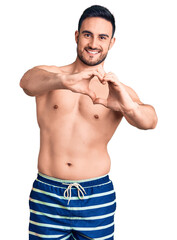Young handsome man wearing swimwear smiling in love doing heart symbol shape with hands. romantic concept.