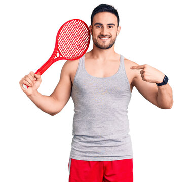 Young handsome man holding tennis racket pointing finger to one self smiling happy and proud