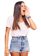 Young hispanic woman wearing casual white tshirt shouting and screaming loud to side with hand on mouth. communication concept.