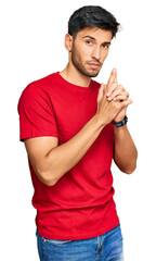 Young handsome man wearing casual red tshirt holding symbolic gun with hand gesture, playing...