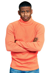 Young black man wearing orange turtleneck sweater skeptic and nervous, disapproving expression on face with crossed arms. negative person.