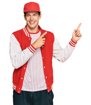 Handsome caucasian man wearing baseball uniform smiling and looking at the camera pointing with two hands and fingers to the side.
