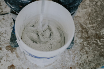 A young man mixes putty with a construction mixer in a bucket.