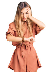 Beautiful caucasian woman with blonde hair wearing summer jumpsuit looking at the watch time worried, afraid of getting late