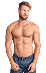 Young caucasian man standing shirtless smiling looking to the side and staring away thinking.