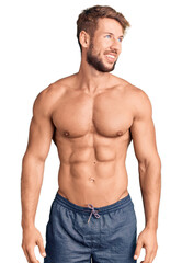 Fototapeta premium Young caucasian man standing shirtless looking away to side with smile on face, natural expression. laughing confident.