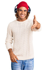 Young hispanic man listening to music using headphones smiling friendly offering handshake as greeting and welcoming. successful business.