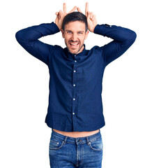 Young handsome man wearing casual shirt posing funny and crazy with fingers on head as bunny ears, smiling cheerful