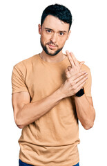 Hispanic man with beard wearing casual t shirt holding symbolic gun with hand gesture, playing killing shooting weapons, angry face