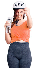 Young beautiful woman wearing bike helmet and holding water bottle annoyed and frustrated shouting with anger, yelling crazy with anger and hand raised