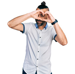 Hispanic man with ponytail wearing casual white shirt doing heart shape with hand and fingers smiling looking through sign