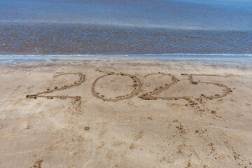 2025 written in the sand on the beach with the sea wave approaching.