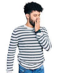 Young arab man with beard wearing casual striped sweater bored yawning tired covering mouth with hand. restless and sleepiness.