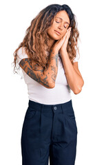 Young hispanic woman with tattoo wearing casual white tshirt sleeping tired dreaming and posing with hands together while smiling with closed eyes.