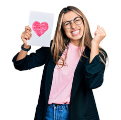Hispanic young woman holding heart draw screaming proud, celebrating victory and success very...