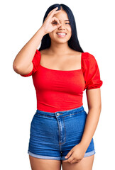 Fototapeta premium Young beautiful asian girl wearing casual clothes doing ok gesture with hand smiling, eye looking through fingers with happy face.