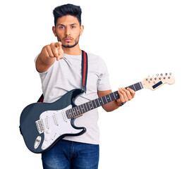 Obraz premium Handsome latin american young man playing electric guitar pointing with finger to the camera and to you, confident gesture looking serious