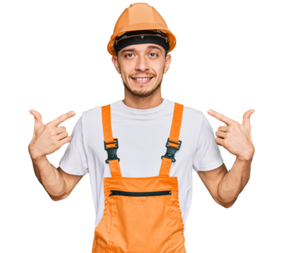 Hispanic young man wearing handyman uniform and safety hardhat looking confident with smile on face, pointing oneself with fingers proud and happy.