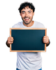 Hispanic young man with beard holding blackboard smiling and laughing hard out loud because funny crazy joke.