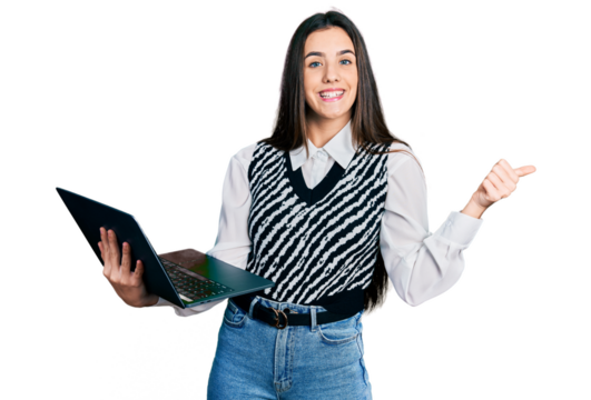 Young brunette teenager working using computer laptop pointing thumb up to the side smiling happy with open mouth
