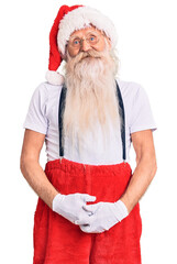 Old senior man with grey hair and long beard wearing santa claus costume with suspenders looking positive and happy standing and smiling with a confident smile showing teeth