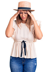 Young beautiful woman wearing summer hat and t-shirt with hand on head for pain in head because stress. suffering migraine.