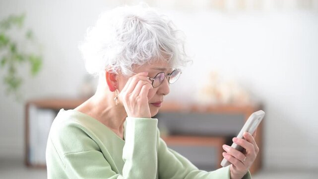 スマートフォン(スマホ)を持つ笑顔のシニア女性　老眼でスマホが見えにくい動画