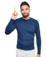 Naklejka premium Young man with beard wearing casual blue winter sweater pointing finger up with successful idea. exited and happy. number one.