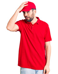 Young handsome man with beard wearing delivery uniform surprised with hand on head for mistake,...