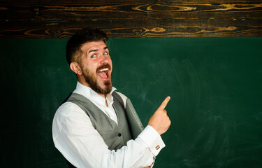 Happy bearded teacher or student with laptop pointing finger at blackboard at copy space. University exam. Male teacher giving lesson to students in classroom. Education in high school or college.