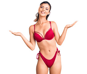 Obraz premium Young beautiful woman wearing bikini smiling showing both hands open palms, presenting and advertising comparison and balance