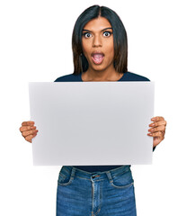 Naklejka premium Young latin transsexual transgender woman holding blank empty banner scared and amazed with open mouth for surprise, disbelief face