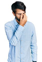 Hispanic man with blue eyes wearing business shirt tired rubbing nose and eyes feeling fatigue and headache. stress and frustration concept.