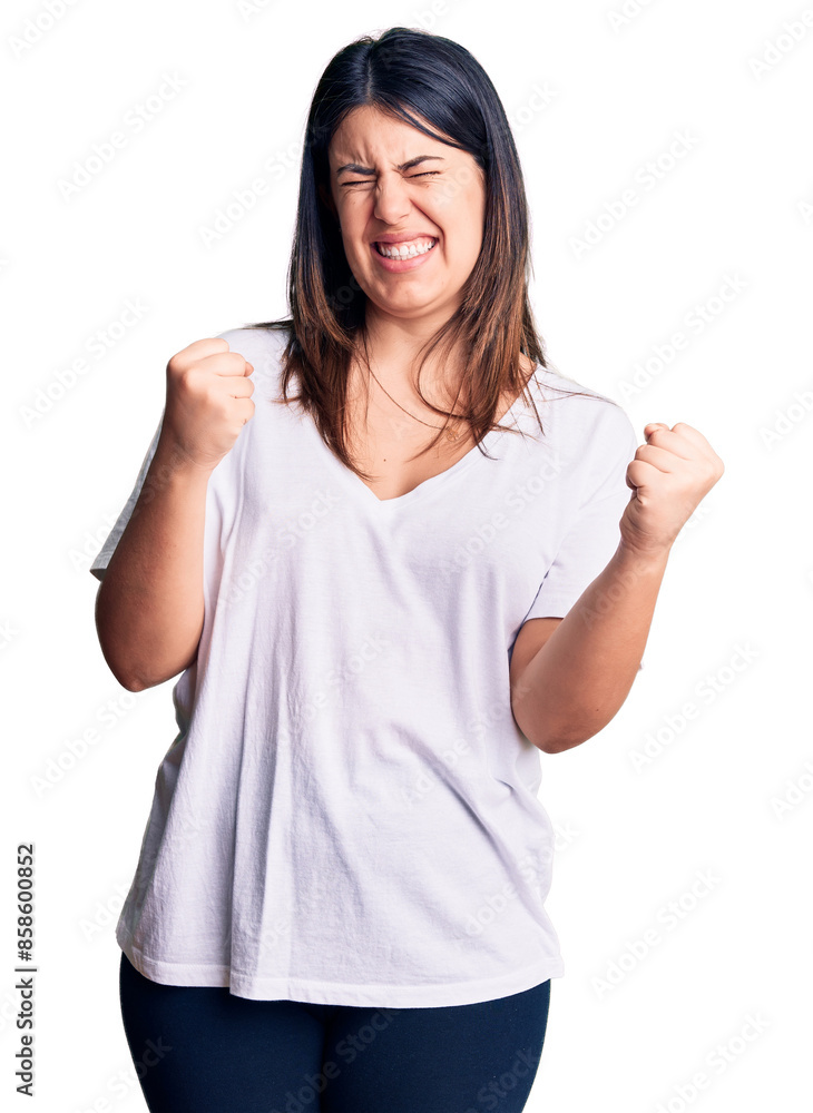 Wall mural Young beautiful brunette woman wearing casual t-shirt very happy and excited doing winner gesture with arms raised, smiling and screaming for success. celebration concept.