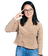 Young chinese woman wearing casual sweater and glasses smiling pointing to head with one finger, great idea or thought, good memory