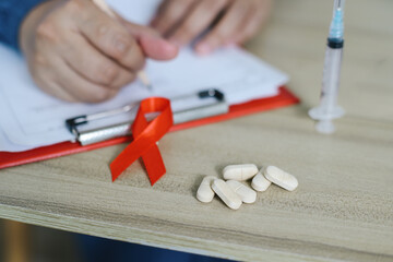 Red Ribbon, Medicine, Syringe And Doctor Writing On Medical Report.