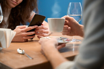 Couple in a restaurant while woman with phone, man holds coffee in his hand