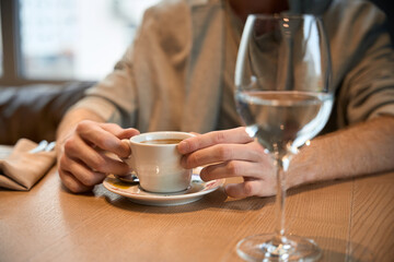 Close up of man holding cup of coffee in restaurant. Glass of water nearby